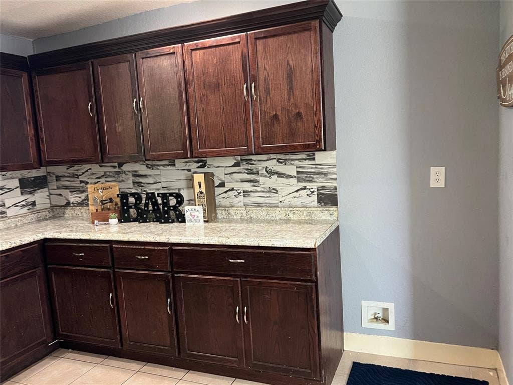 3227 Avenue I, Fort Worth, TX 76105 Dark wood-finish cabinetry with crown molding, light-colored speckled countertops, and a patterned backsplash
