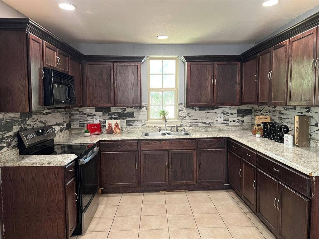 3227 Avenue I, Fort Worth, TX 76105 U-shaped kitchen with dark wood cabinetry, light speckled countertops, a patterned backsplash, stainless steel appliances, and recessed lighting