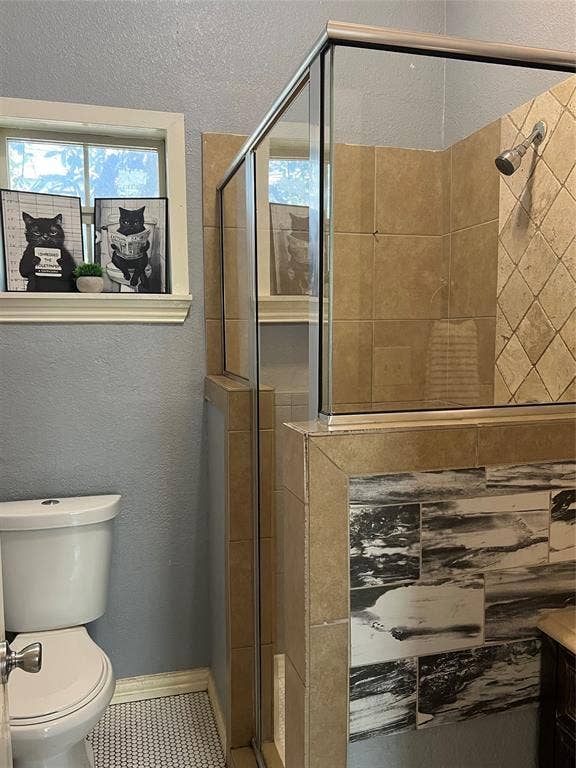 3227 Avenue I, Fort Worth, TX 76105 Glass-enclosed shower with tiled walls, a window with trim, a toilet, and patterned floor tile
