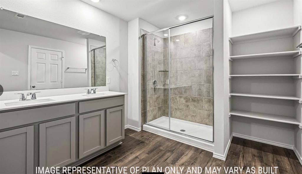 10408 Altair Drive, Waco, TX 76708 Dual vanity with undermount sinks and chrome fixtures, frameless glass shower enclosure with subway tile surround, wood-finish flooring, recessed lighting, and built-in shelving