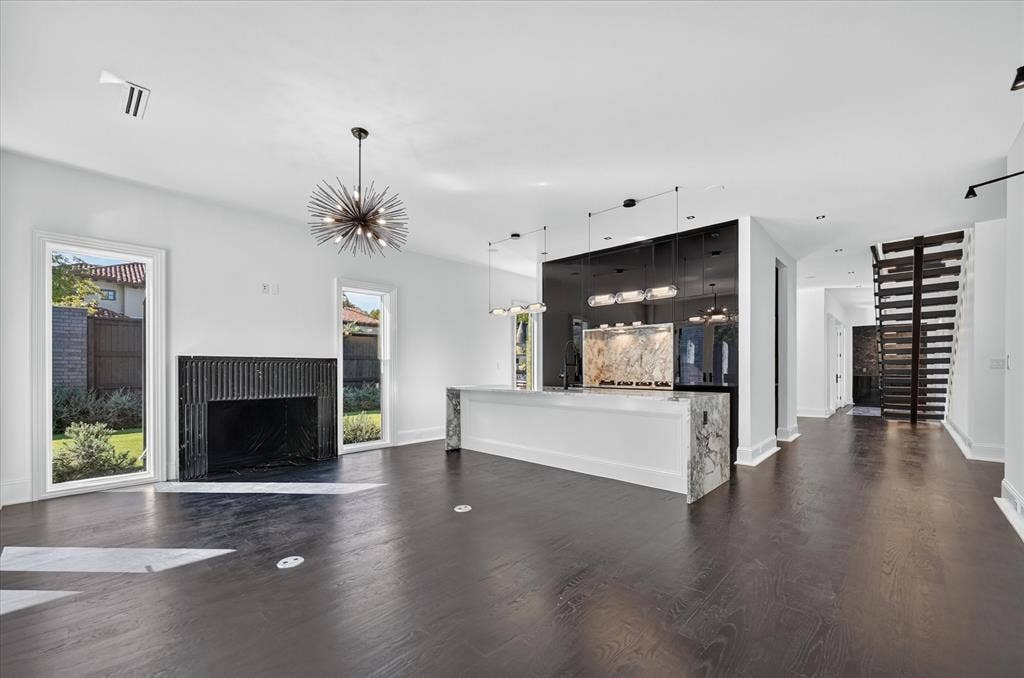 6404 Lakehurst Avenue, Dallas, TX 75230 Dark wood-finish flooring, a fluted black fireplace surround, and a white stone kitchen island with a waterfall edge
