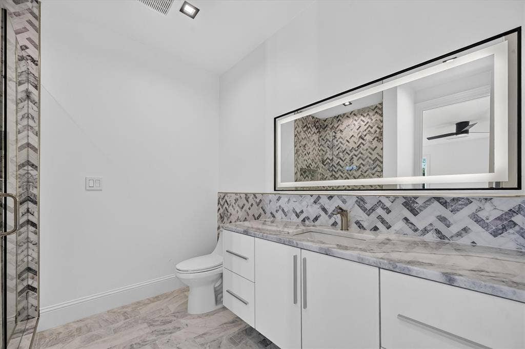 6404 Lakehurst Avenue, Dallas, TX 75230 Modern bathroom featuring a glass-enclosed shower with chevron tile, an illuminated mirror, a vanity with a stone countertop, and wood-finish flooring