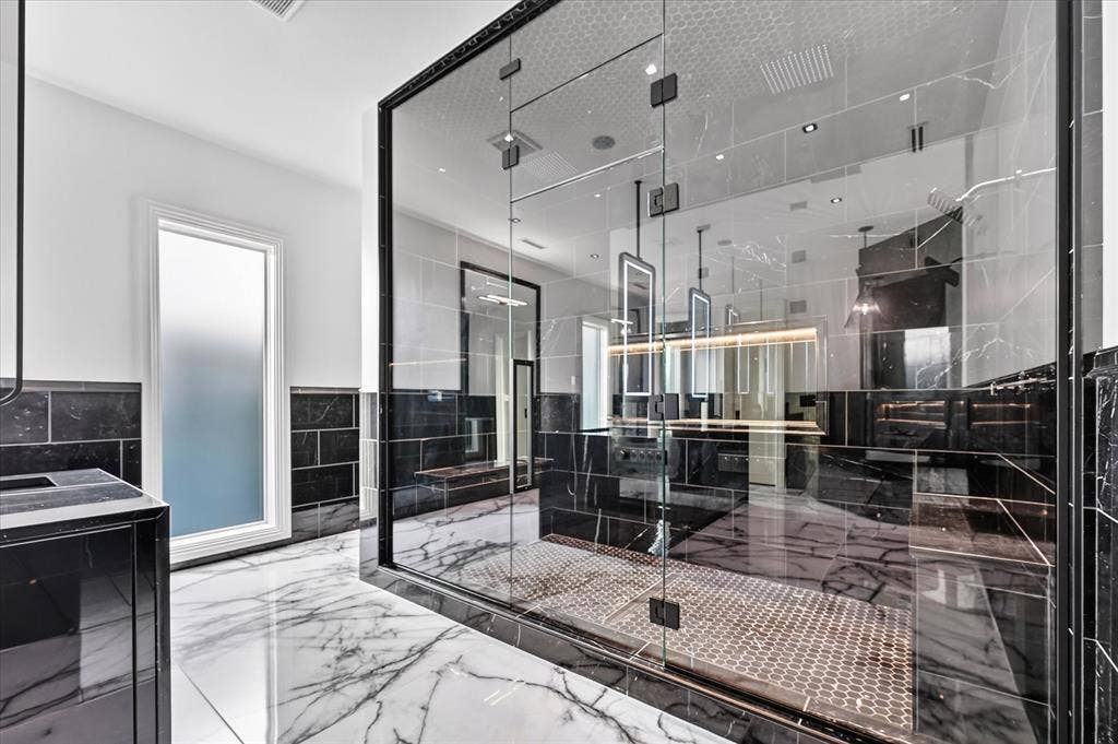 6404 Lakehurst Avenue, Dallas, TX 75230 Spacious bathroom featuring white and black marble-style flooring, a large glass-enclosed shower with honeycomb tile, a frosted privacy window, and dark tiled wainscoting
