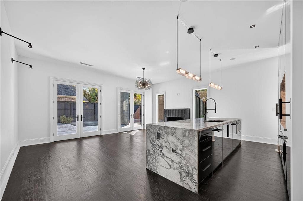 6404 Lakehurst Avenue, Dallas, TX 75230 Spacious room with dark wood-finish flooring, multiple sets of white French doors, and a kitchen island featuring a waterfall stone countertop and integrated sink