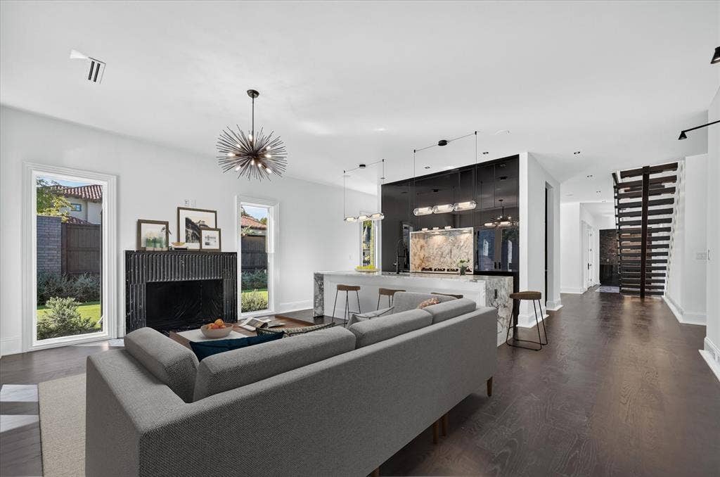 6404 Lakehurst Avenue, Dallas, TX 75230 Open-concept living space featuring wood-finish flooring, a modern black fireplace, an island with stone countertops, and a unique open staircase design