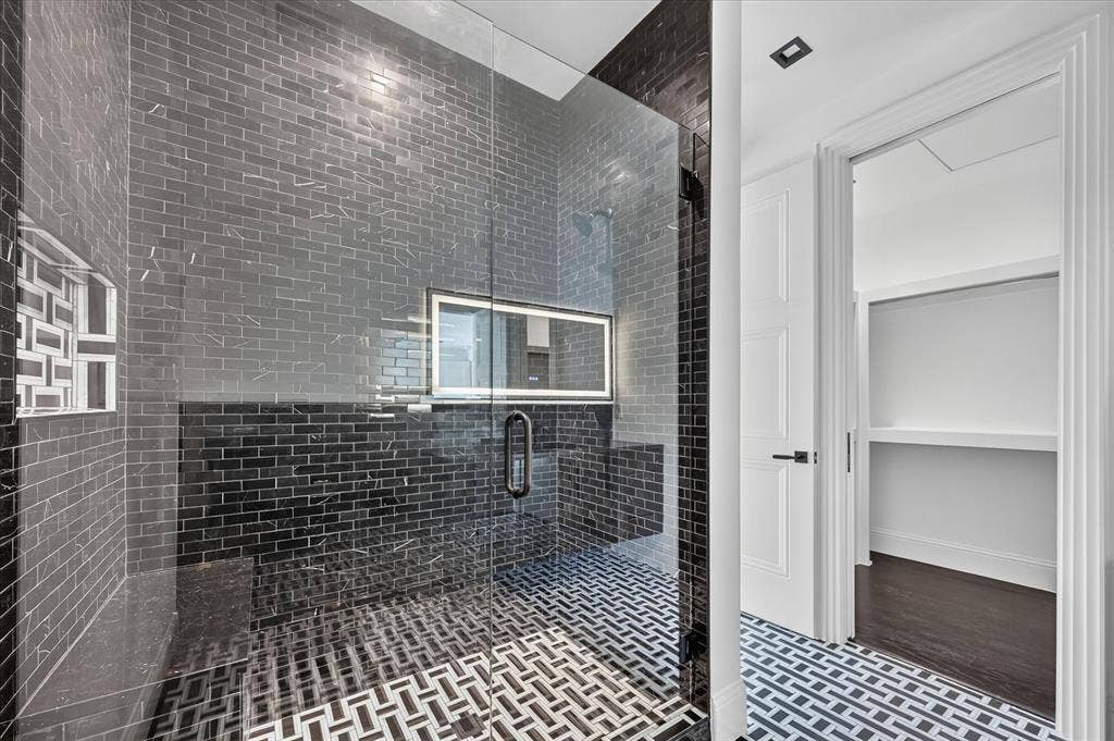 6404 Lakehurst Avenue, Dallas, TX 75230 Glass-enclosed shower with black subway tile, mosaic floor tile, and a built-in shower niche