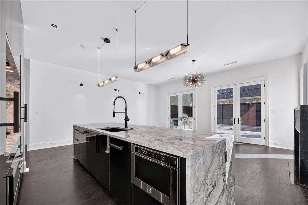 6404 Lakehurst Avenue, Dallas, TX 75230 Gourmet kitchen featuring a waterfall island with integrated sink, sleek black cabinetry, dark wood-finish flooring, and multiple pendant light fixtures