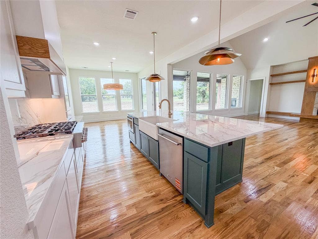 3860 Jacks Loop, Midlothian, TX 76065 Open-concept kitchen with a large island featuring a farmhouse sink, stainless steel appliances, marble-look countertops, and wood-finish flooring