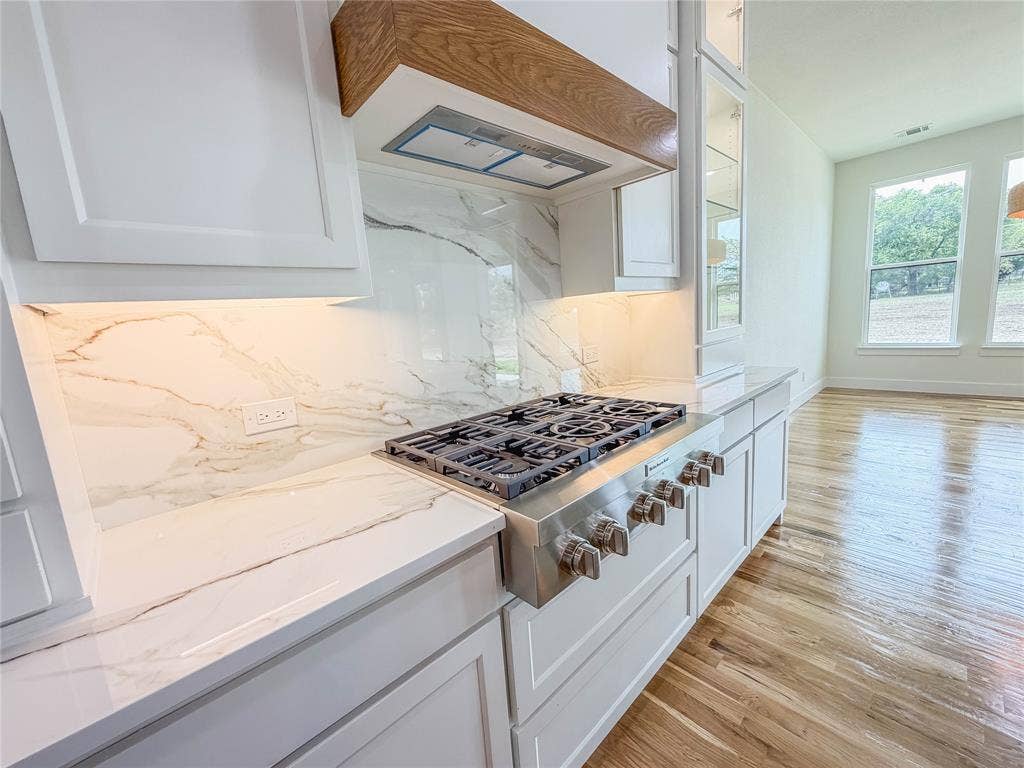 3860 Jacks Loop, Midlothian, TX 76065 Gourmet kitchen featuring a built-in gas range, wood-finish range hood, white shaker cabinetry, and a marbled backsplash