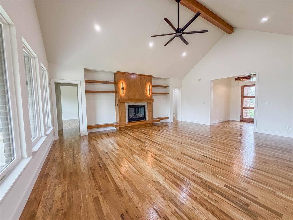 3860 Jacks Loop, Midlothian, TX 76065 Vaulted ceiling with an exposed wood beam, large ceiling fan, recessed lighting, wood-finish flooring, and a fireplace with wood paneling and built-in shelving