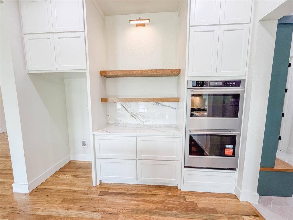 3860 Jacks Loop, Midlothian, TX 76065 White shaker cabinetry, wood-finish flooring, built-in double ovens, marble-look backsplash, and floating wood shelves