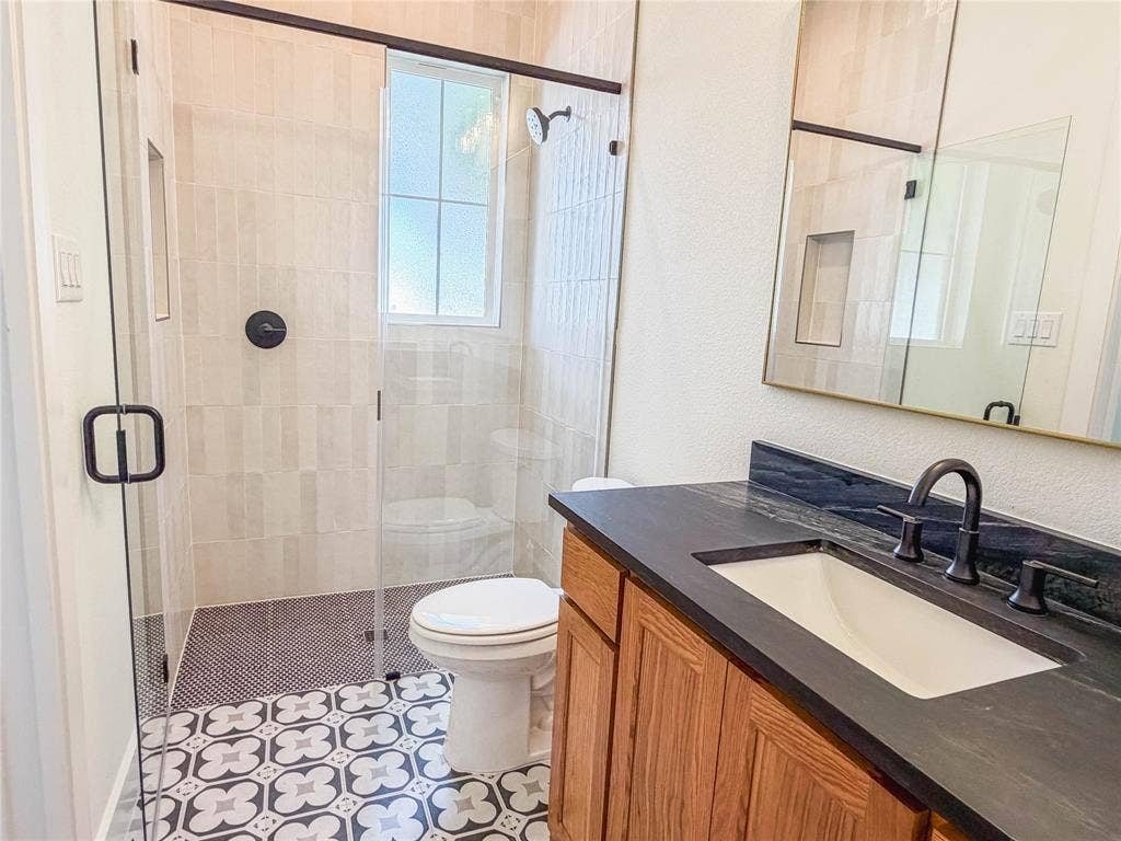 3860 Jacks Loop, Midlothian, TX 76065 Walk-in shower with clear glass enclosure and black hardware, patterned floor tile, single vanity with dark countertop, and rectangular undermount sink