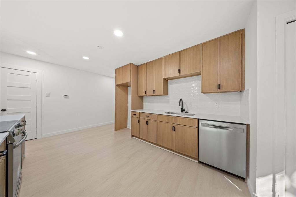 Kitchen featuring wood-finish cabinetry, neutral solid-surface countertops, a stainless steel dishwasher, a matte black faucet, and recessed lighting