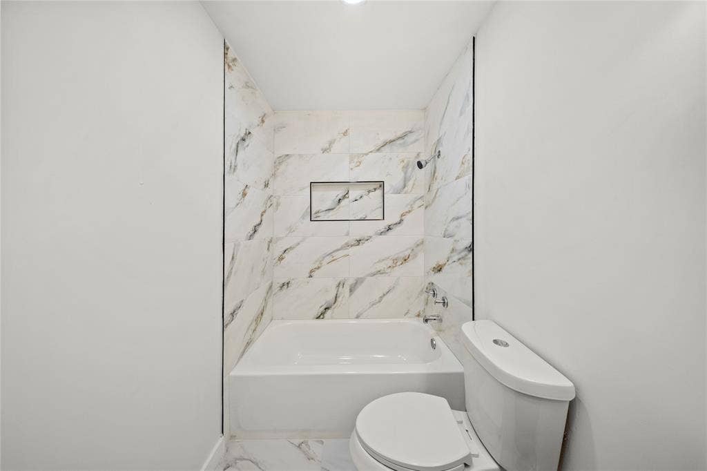 Full-height wall surround with stone-finish porcelain tile, integrated recessed shelving, and a white soaking tub featuring polished chrome plumbing fixtures