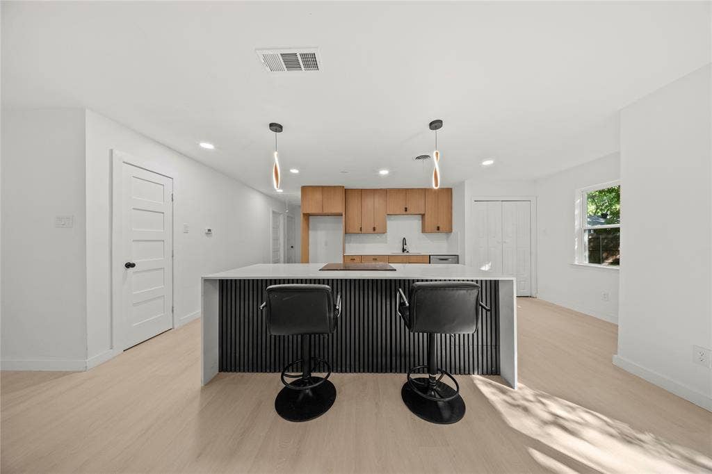 Kitchen featuring wood-finish cabinetry, a central island with a waterfall countertop and vertical slat detailing, integrated lighting, and light-toned wood-finish flooring