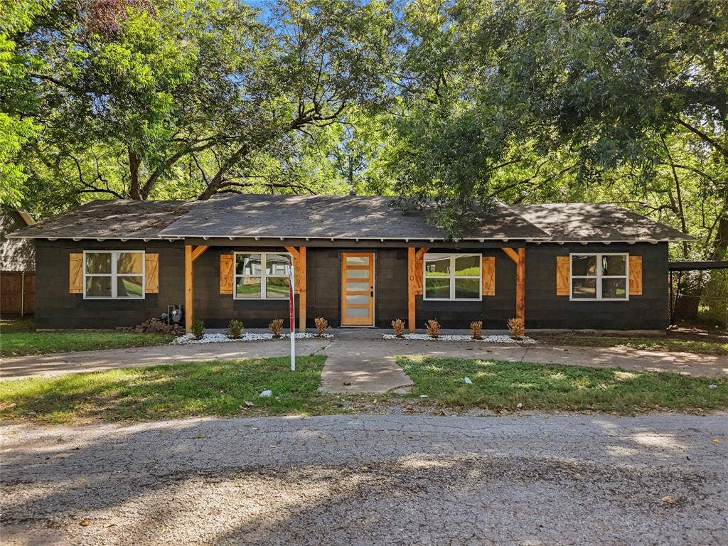 Exterior facade featuring dark-toned horizontal siding, wood-finish window shutters, exposed timber support beams, and a modern glass-paneled entry door
