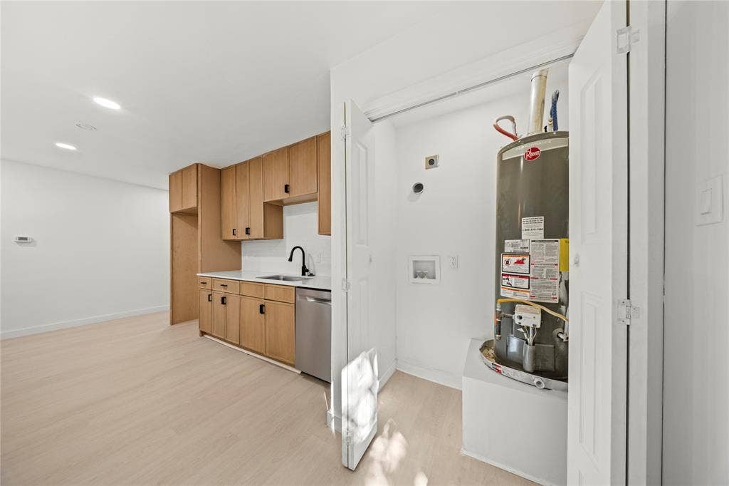 Kitchenette featuring wood-finish cabinetry, white countertops, a stainless steel dishwasher, and a matte black faucet, complemented by wood-finish flooring