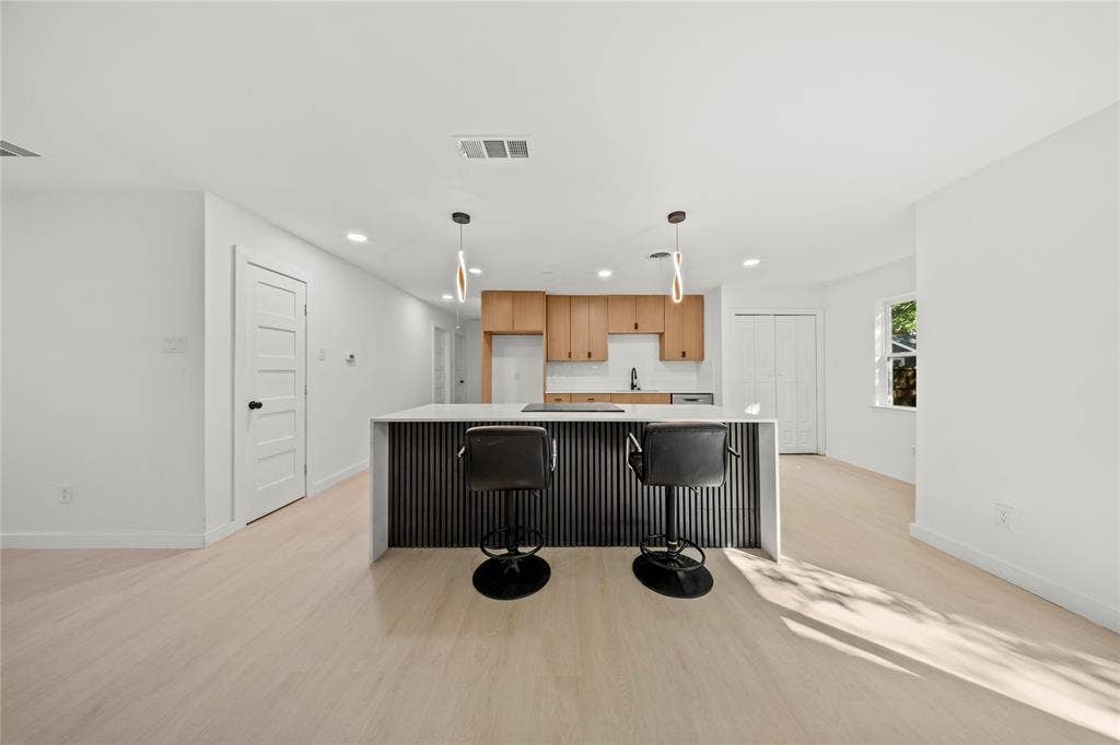 Kitchen featuring light wood-finish cabinetry, a central island with a ribbed facade, integrated cooktop, recessed lighting, and wood-finish flooring