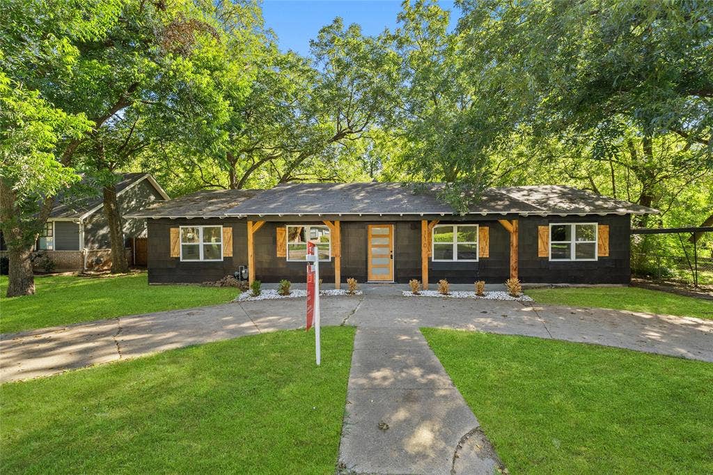 Single-story exterior featuring dark lap siding, wood-toned shutters, a covered front porch with timber support beams, and a modern multi-pane entry door