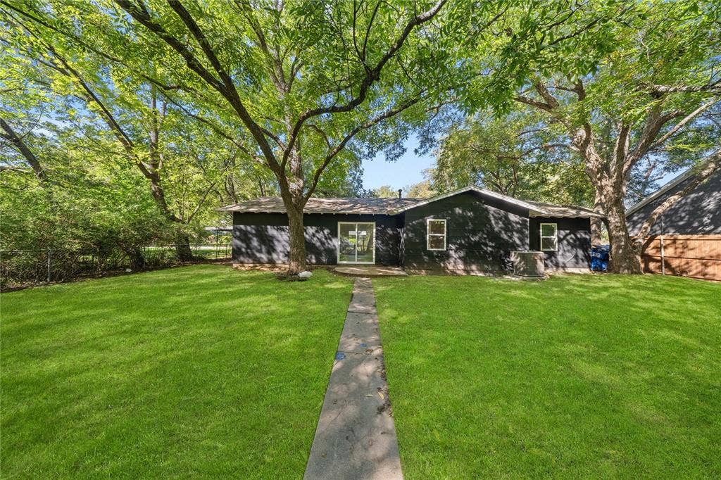 Expansive backyard featuring a manicured lawn, mature trees, concrete pathway, and horizontal wood-finish siding