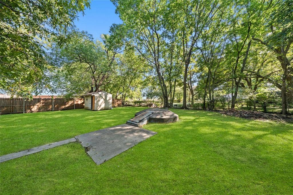 Expansive backyard featuring mature trees, a wood privacy fence, a detached storage structure, and a concrete storm shelter