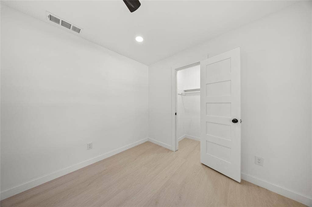Room featuring wood-finish flooring, recessed lighting, and a five-panel interior door with matte black hardware, providing entry to a walk-in closet with built-in shelving