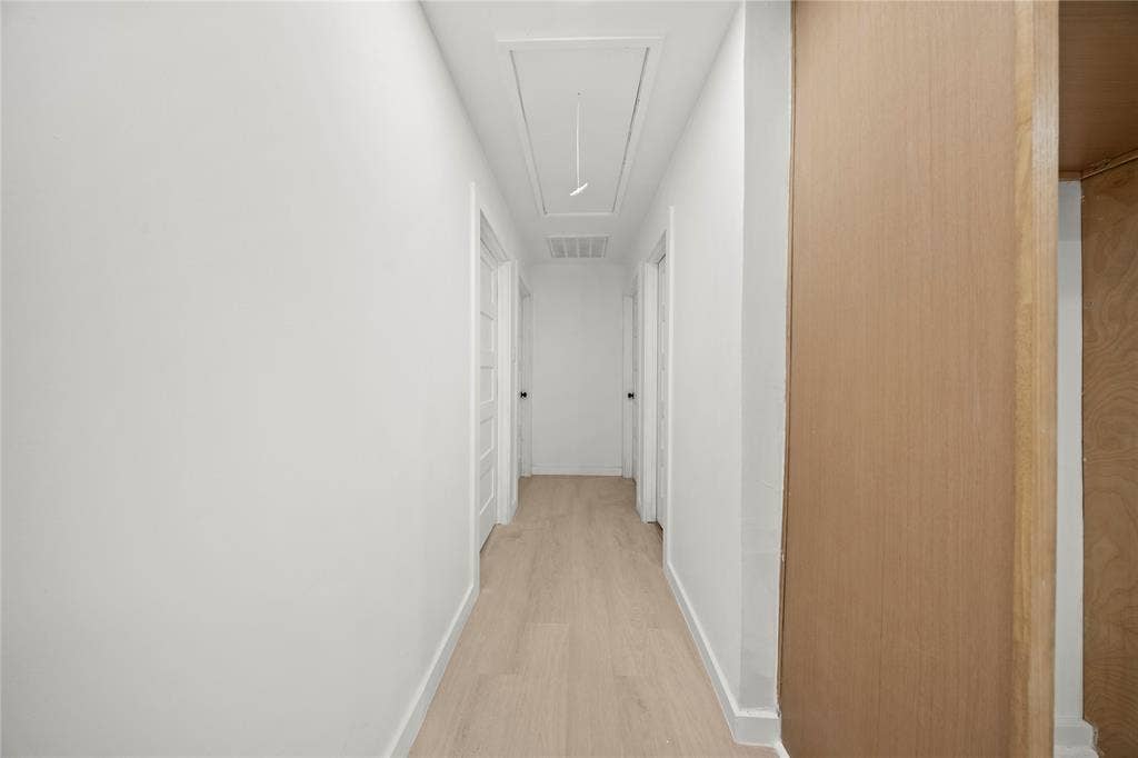 Hallway featuring wood-finish flooring, white walls, and multiple interior doors