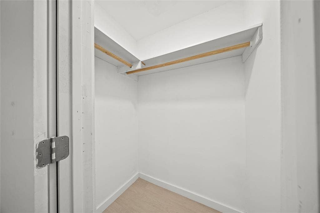 Walk-in closet featuring white walls, wood-finish flooring, and integrated wrap-around shelving with wood hanging rods