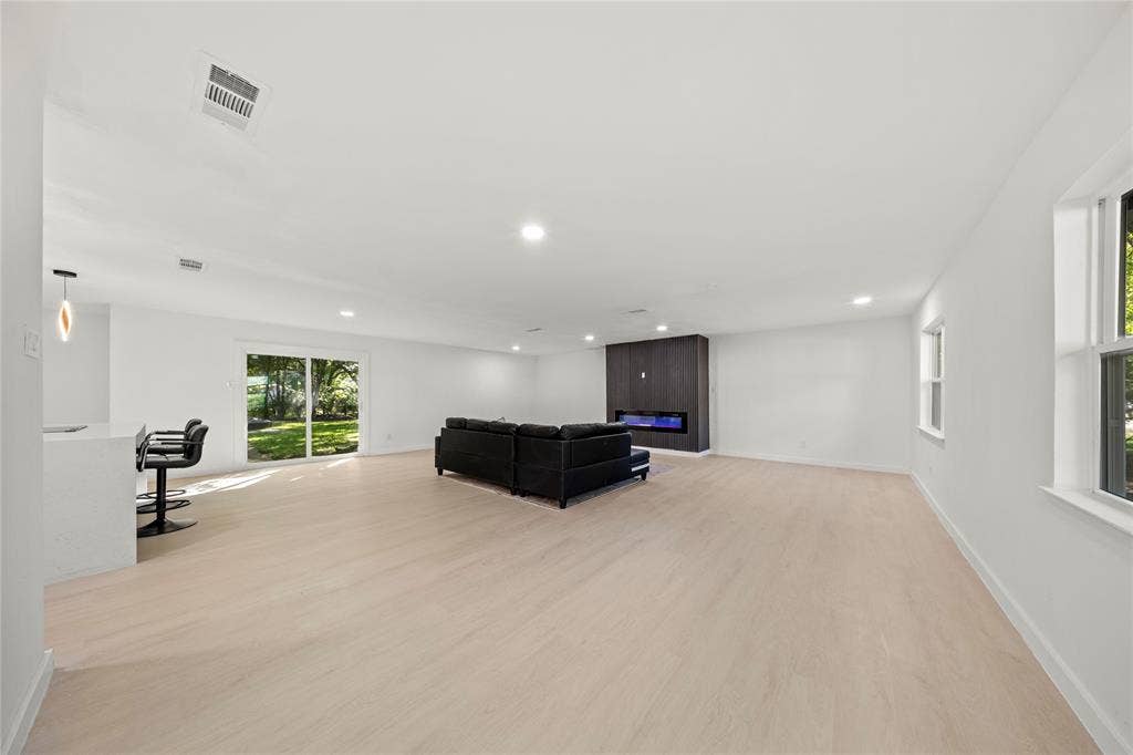Open-concept interior featuring wood-finish flooring, recessed lighting, a modern floor-to-ceiling fireplace surround with integrated electric insert, and sliding glass doors