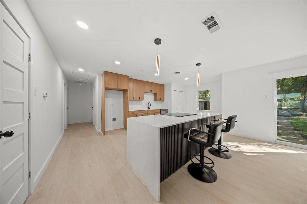 Kitchen featuring wood-finish cabinetry, a waterfall-edge island with a vertical-slat base, neutral solid-surface countertops, recessed lighting, and wood-finish flooring