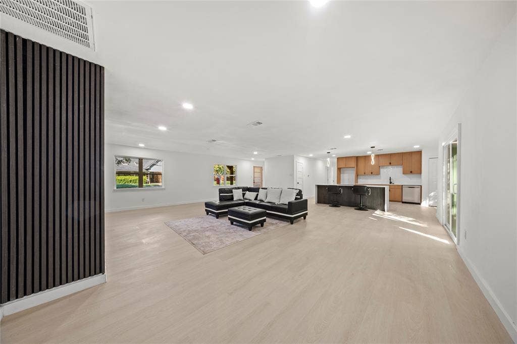 Open floor plan featuring light wood-finish flooring, a vertical-slat accent wall, recessed lighting, and a kitchen island with built-in cabinetry