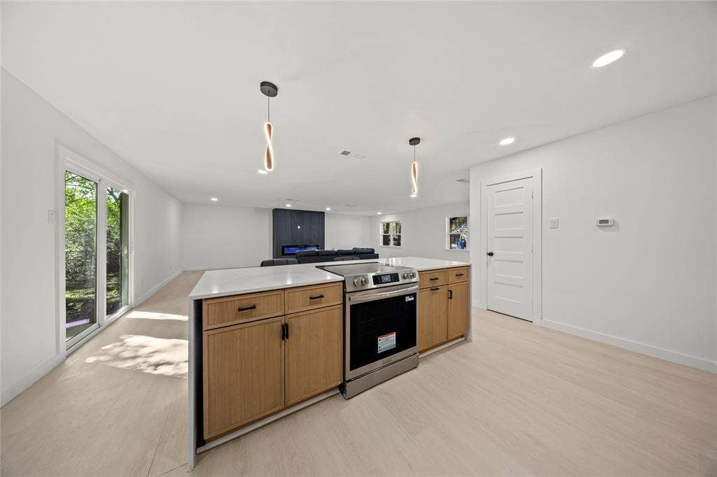 Kitchen featuring an island with light wood-finish cabinetry, a solid surface countertop, stainless steel electric range, dual pendant lighting, and light wood-finish flooring