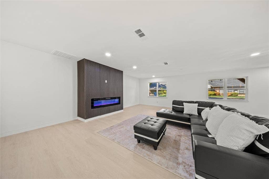 Living space featuring light wood-finish flooring, recessed lighting, and a floor-to-ceiling dark wood-slatted feature wall with an integrated linear electric fireplace