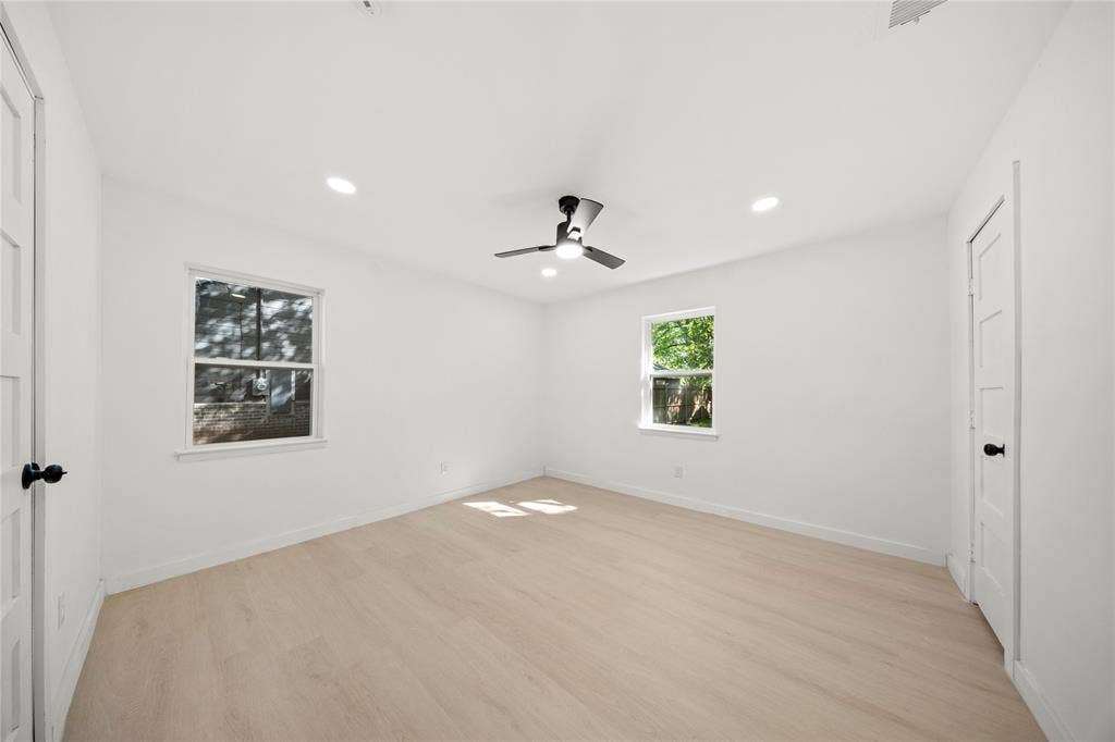 Neutral-toned room featuring light wood-finish flooring, recessed lighting, a ceiling fan with integrated lighting, and dual windows