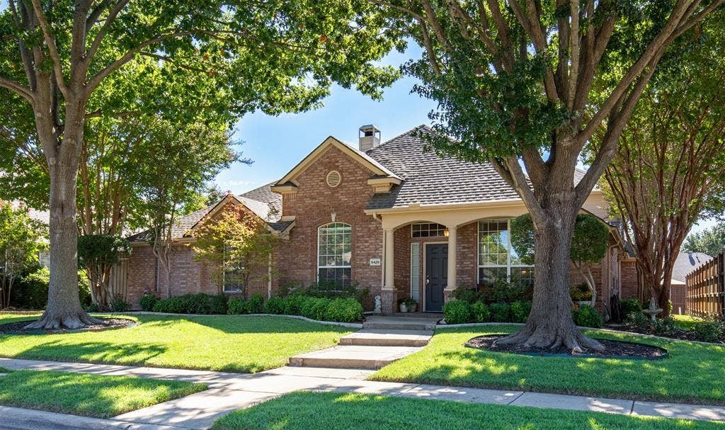 Beautiful curb appeal with mature trees, offering shade, and bordered lush landscaping.