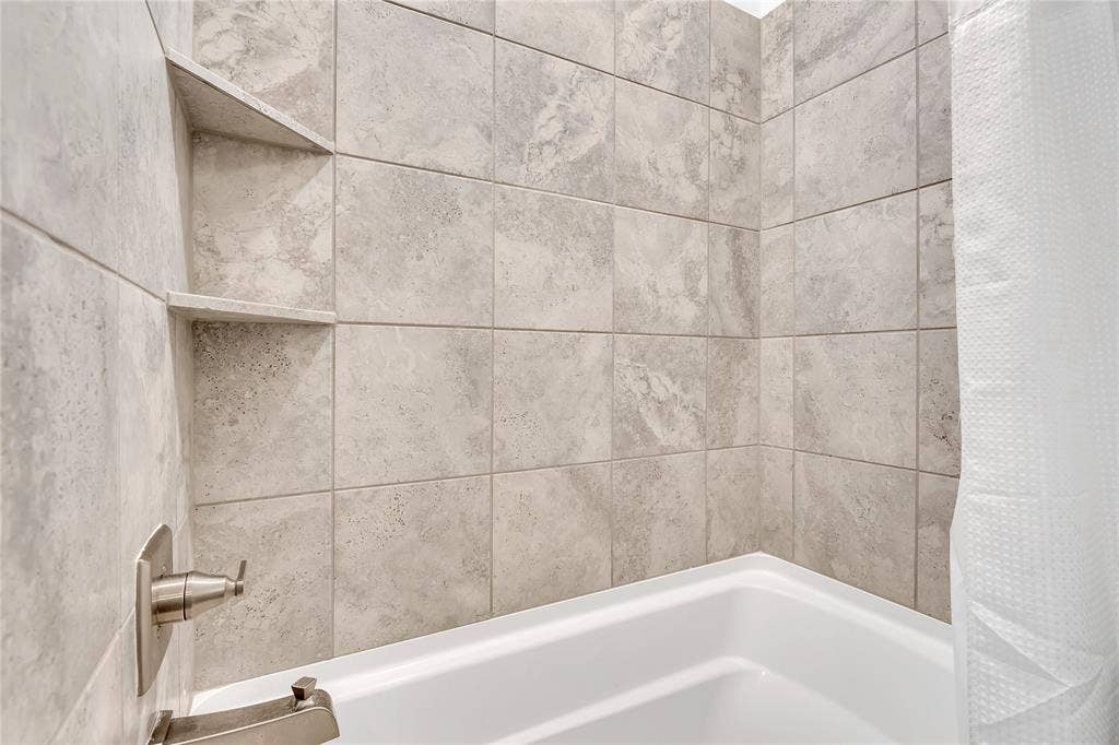 525 Division Street, Plano, TX 75075 Bathtub with neutral-toned wall tiles, two recessed corner shelves, and brushed metal fixtures