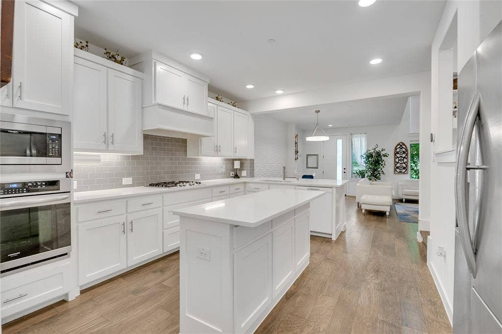 525 Division Street, Plano, TX 75075 Modern kitchen featuring an island, white cabinetry, integrated stainless steel appliances, a tile backsplash, and wood-finish flooring