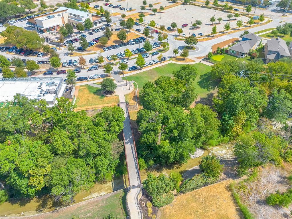 525 Division Street, Plano, TX 75075 Aerial perspective highlighting a pedestrian bridge spanning a natural waterway, surrounded by mature trees and manicured green spaces