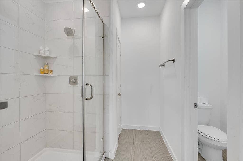 525 Division Street, Plano, TX 75075 Glass-enclosed shower with tile surround and built-in shelving, complemented by recessed lighting and a towel bar