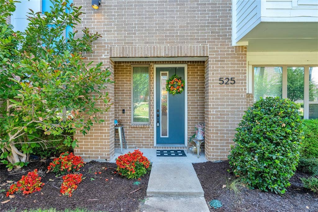 525 Division Street, Plano, TX 75075 Brick exterior with a prominent entry, modern address numbers, and a landscaped front yard featuring mature shrubs and vibrant red plantings