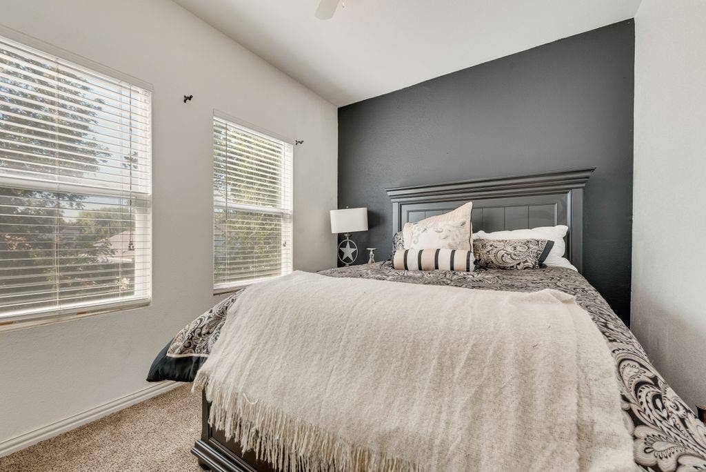 Vaulted ceiling, two windows with blinds, carpeted flooring, and an accent wall