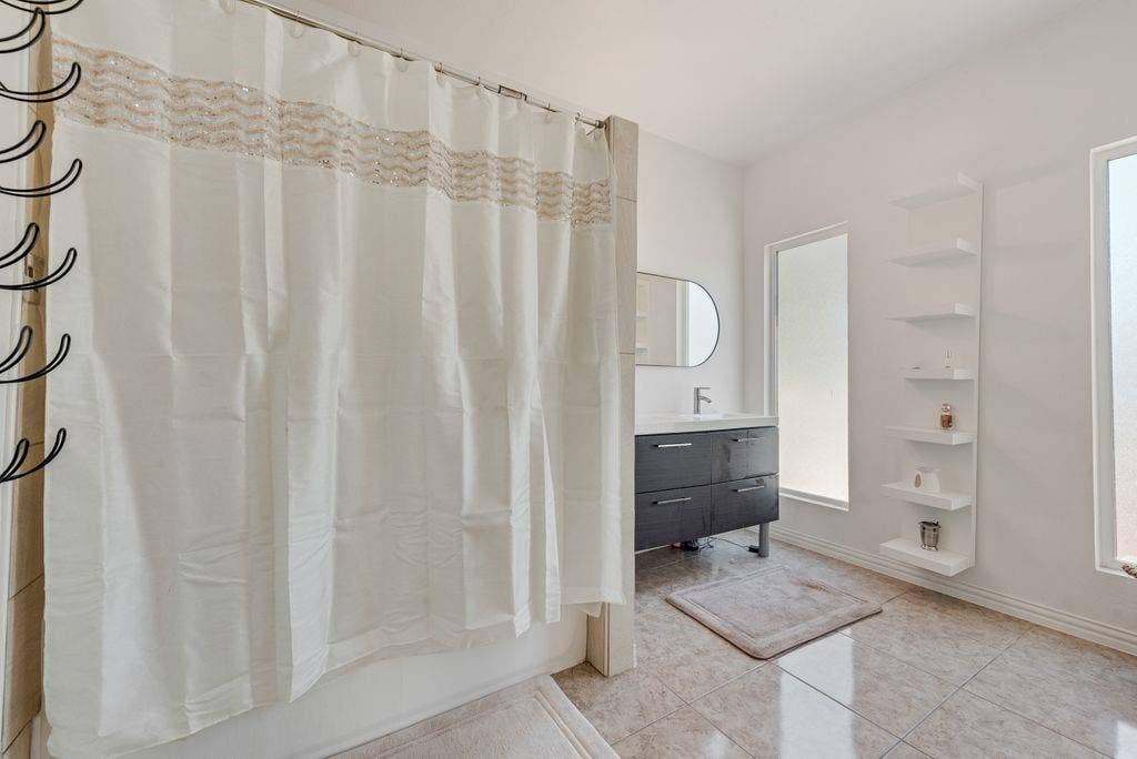 Tile flooring, modern vanity with integrated sink, contemporary wall-mounted mirror, multiple vertical windows, built-in shelving