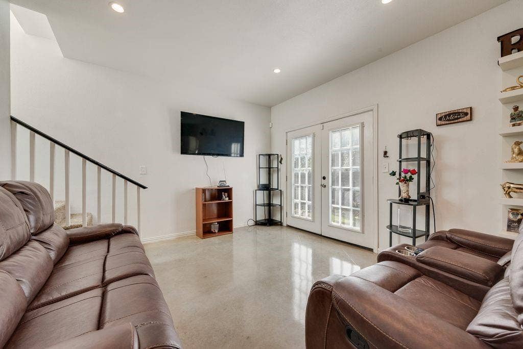 Recessed lighting, light-toned flooring, staircase with dark handrail and white balusters, and white French doors with divided lites