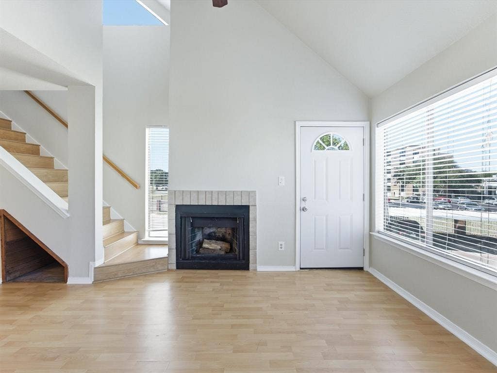 3129 Sondra Drive, #206, Fort Worth, TX 76107 Vaulted ceiling, wood-finish flooring, brick-surround fireplace, large window with blinds, and a staircase with wood handrails