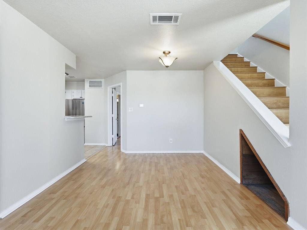 3129 Sondra Drive, #206, Fort Worth, TX 76107 Wood-finish flooring throughout, staircase with wood treads and white risers, under-stair storage nook, and ceiling-mounted light fixture