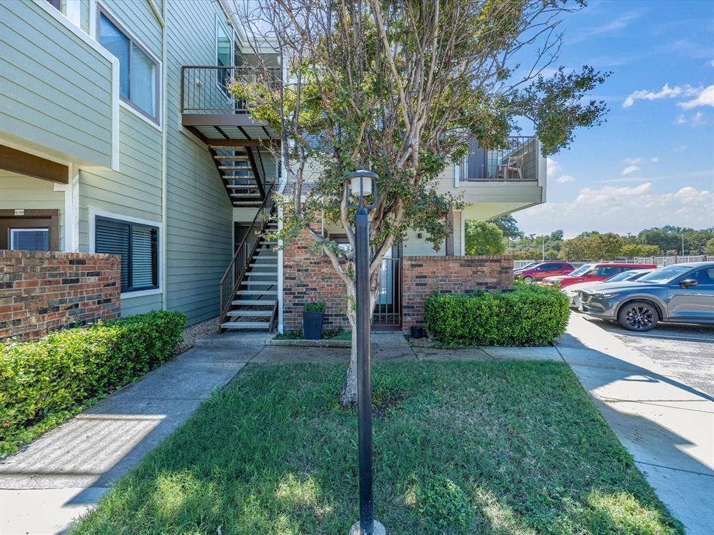 3129 Sondra Drive, #206, Fort Worth, TX 76107 Exterior siding in a light green finish, brick accent wall, and a multi-level structure with an upper balcony featuring a metal railing