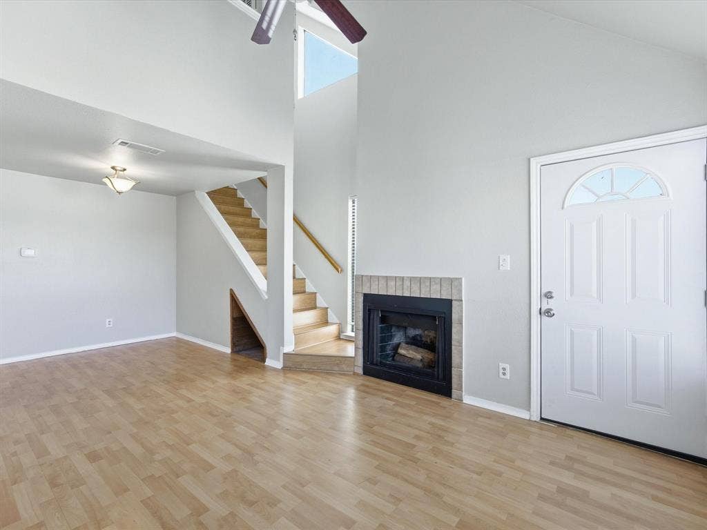 3129 Sondra Drive, #206, Fort Worth, TX 76107 Vaulted ceilings with a ceiling fan, a fireplace with a brick surround, wood-finish flooring, a white paneled entry door with an arched window, and an open staircase with wood handrails