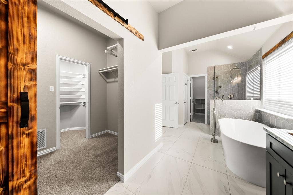 242 Cox Drive, Fate, TX 75087 Freestanding bathtub with floor-mounted faucet, hexagon tile shower surround, wood-finish barn door, and walk-in closet with built-in shelving