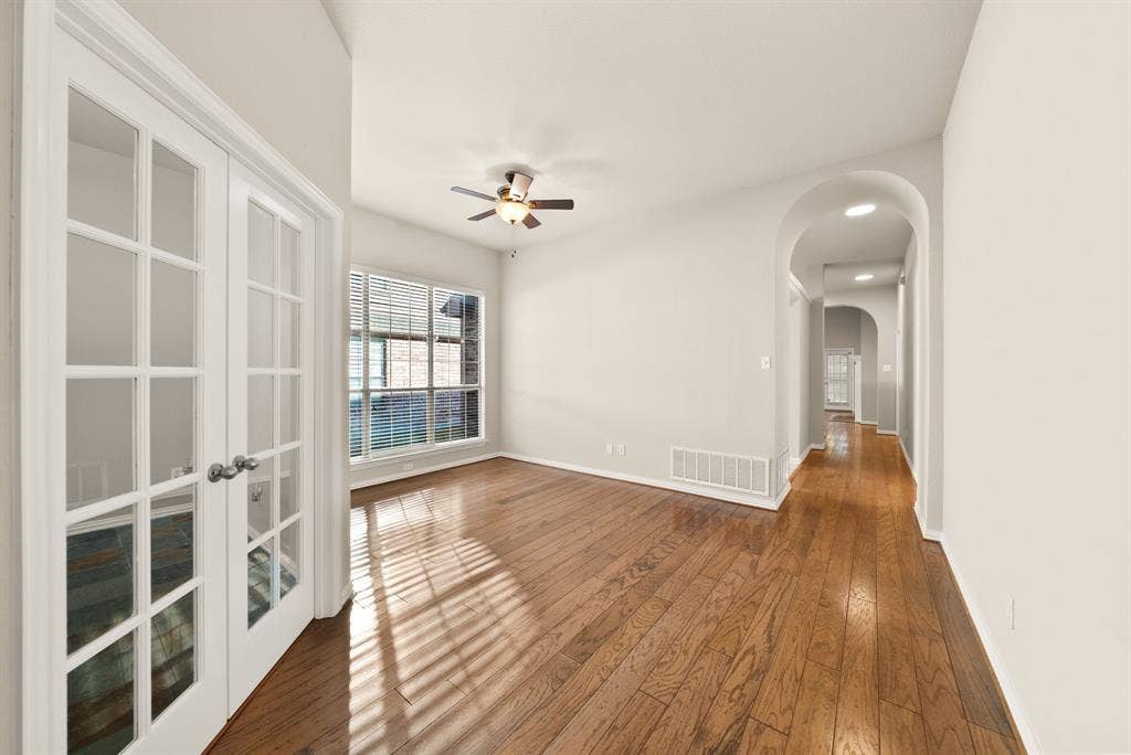 242 Cox Drive, Fate, TX 75087 Hardwood flooring throughout, French doors with glass panels, large window with blinds, ceiling fan with light fixture, and arched hallway entry
