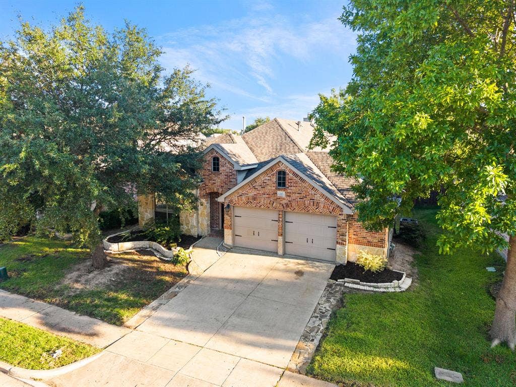 242 Cox Drive, Fate, TX 75087 Elegant brick Colonial with a two-car garage featuring arched doors, situated on a landscaped lot with mature trees and a manicured lawn